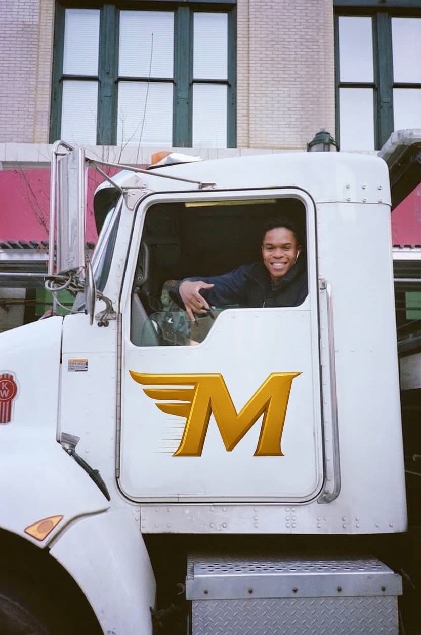 Mark Williams smiling from the cab of a white Marmik Towing & Transport truck with the gold winged M on the door